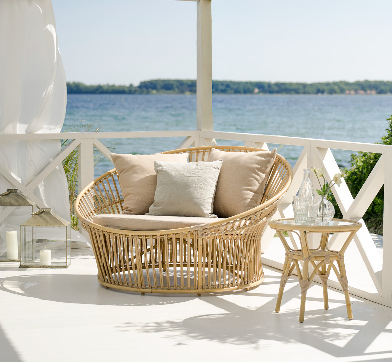 This is a lifestyle image of Tony Exterior Side Table in natural aluminium artfibre. On a wooden deck with jute rug by the sea.