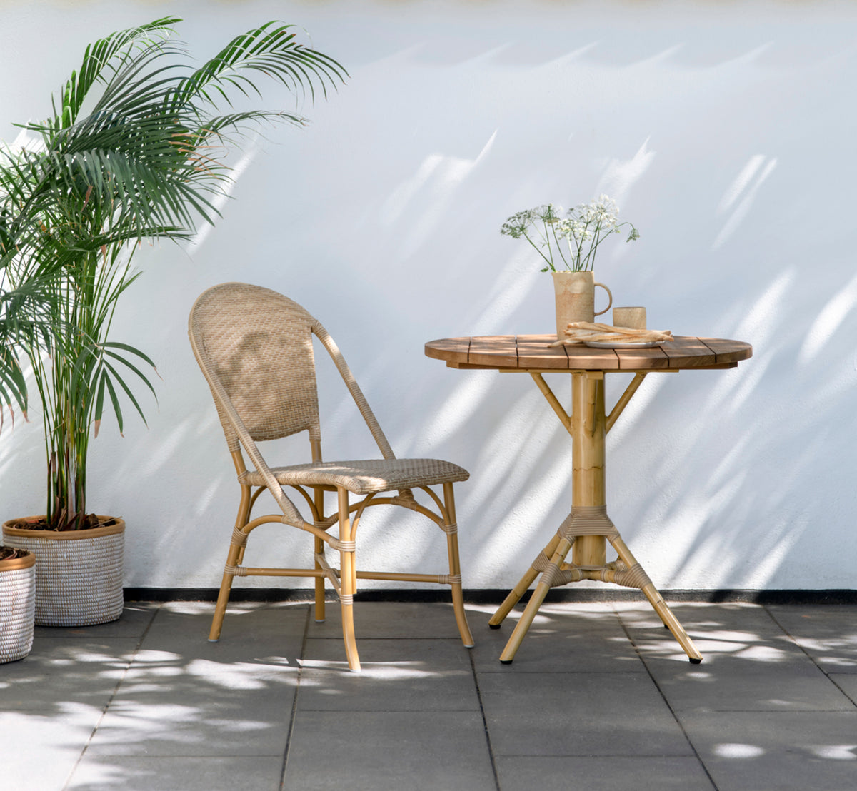 This is a lifestyle image of Nicole Cáfe Table | Teak Ø80 cm in natural aluminium artfibre. Styled in a bright interior setting.