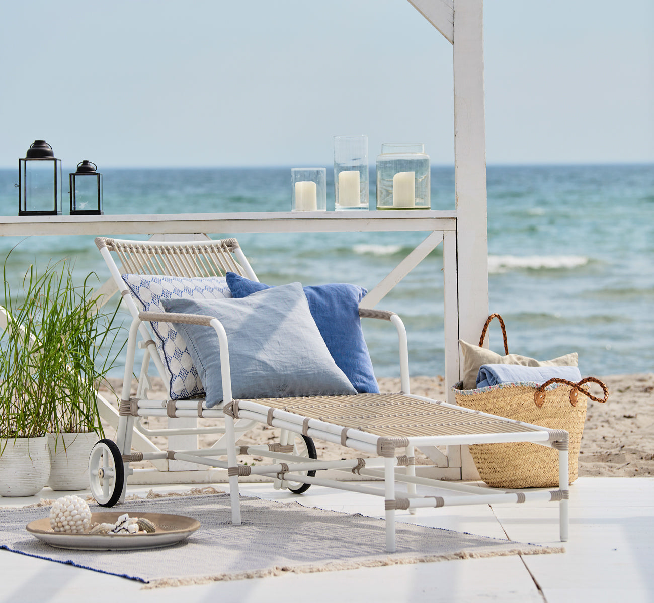 This is a lifestyle image of Josephine sunbed in dove White aluminium artfibre, on a beachside white wooden deck under a white pergola with sea views.