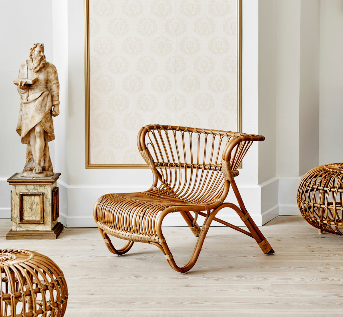 This is a lifestyle image of Fox Lounge Chair in polished Antique Rattan, in a warm interior with ochre wainscoting and dark herringbone parquet.