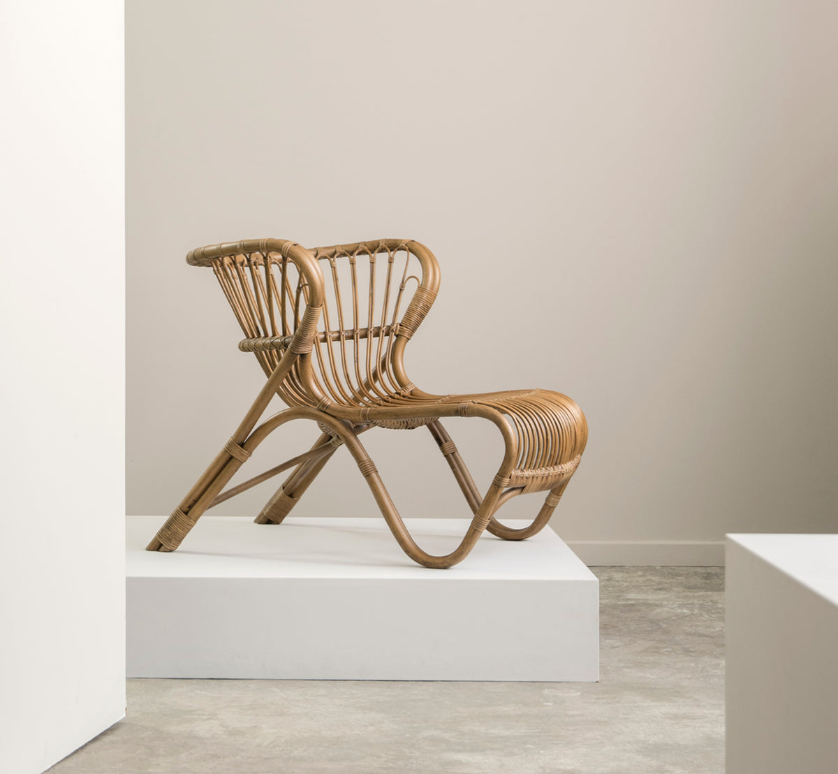 This is a lifestyle image of Fox Lounge Chair in polished Antique Rattan, in a warm interior with ochre wainscoting and dark herringbone parquet.