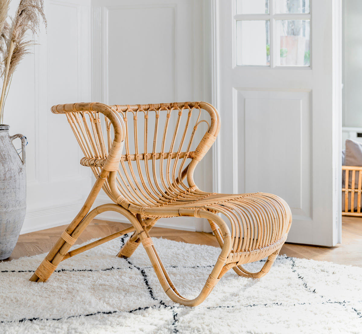 This is a lifestyle image of Fox Lounge Chair in polished Natural Rattan, in a warm interior with ochre wainscoting and dark herringbone parquet.