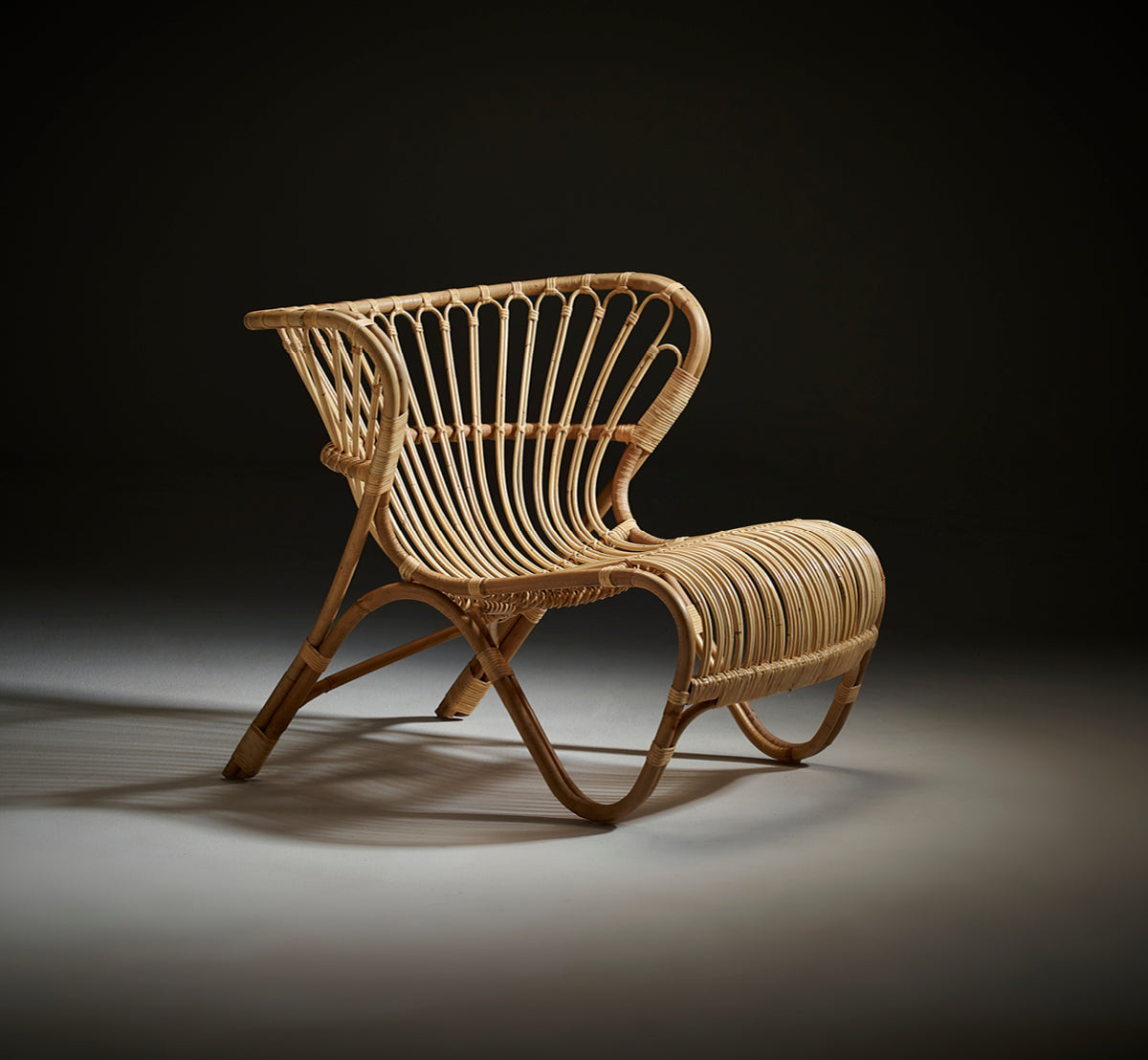 This is a lifestyle image of Fox Lounge Chair in polished Natural Rattan, in a warm interior with ochre wainscoting and dark herringbone parquet.