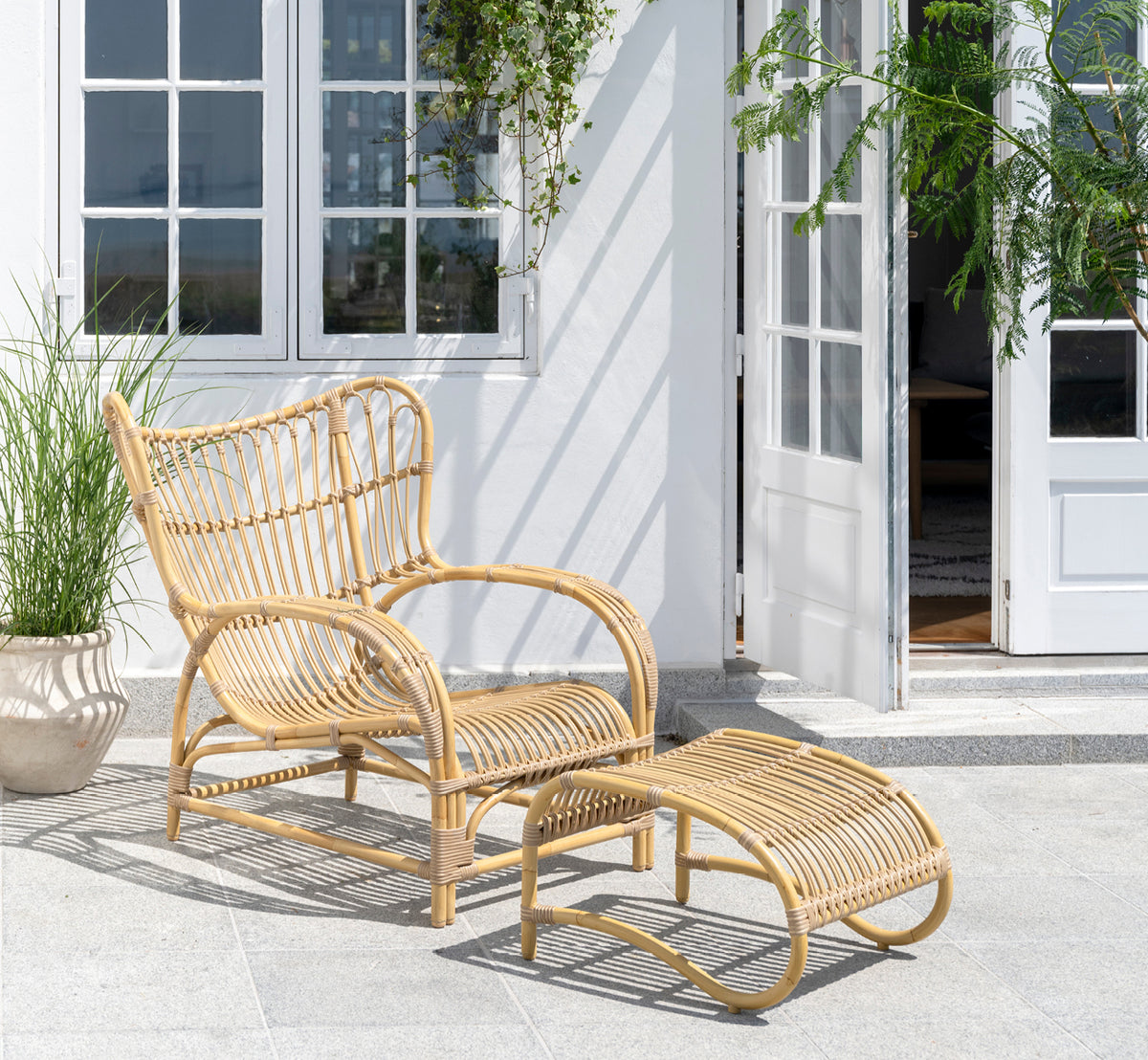 This is a lifestyle image of Teddy Exterior Footstool in natural aluminium artfibre. Paired with the matching lounge chair on a sunny paved terrace.