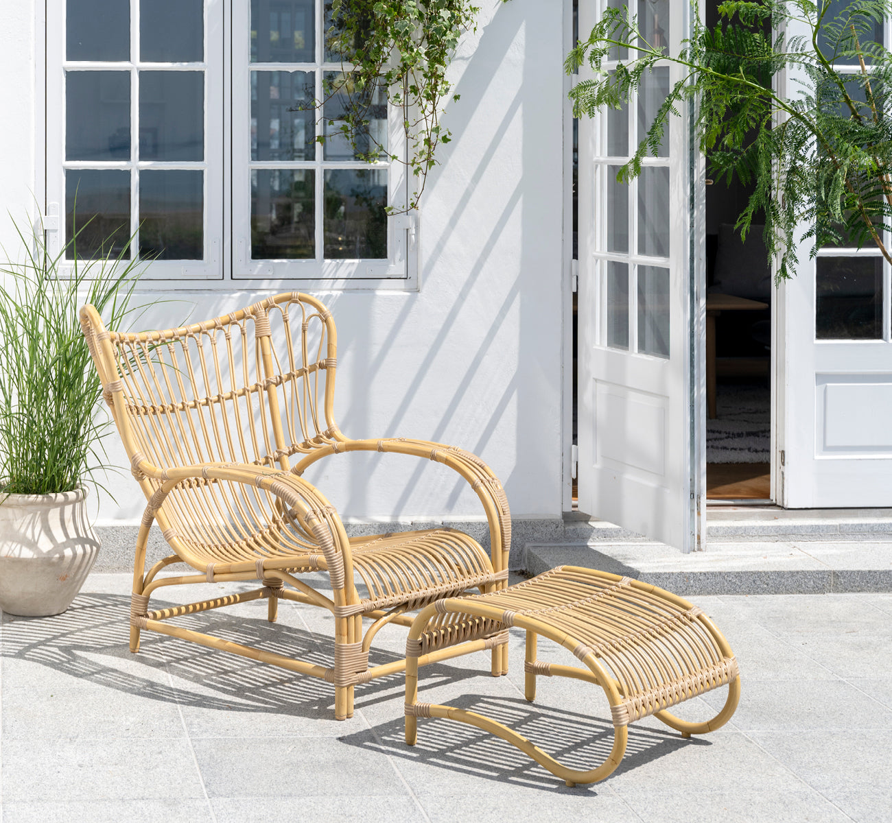 This is a lifestyle image of Teddy Exterior Footstool in natural aluminium artfibre. Paired with the matching lounge chair on a sunny paved terrace.