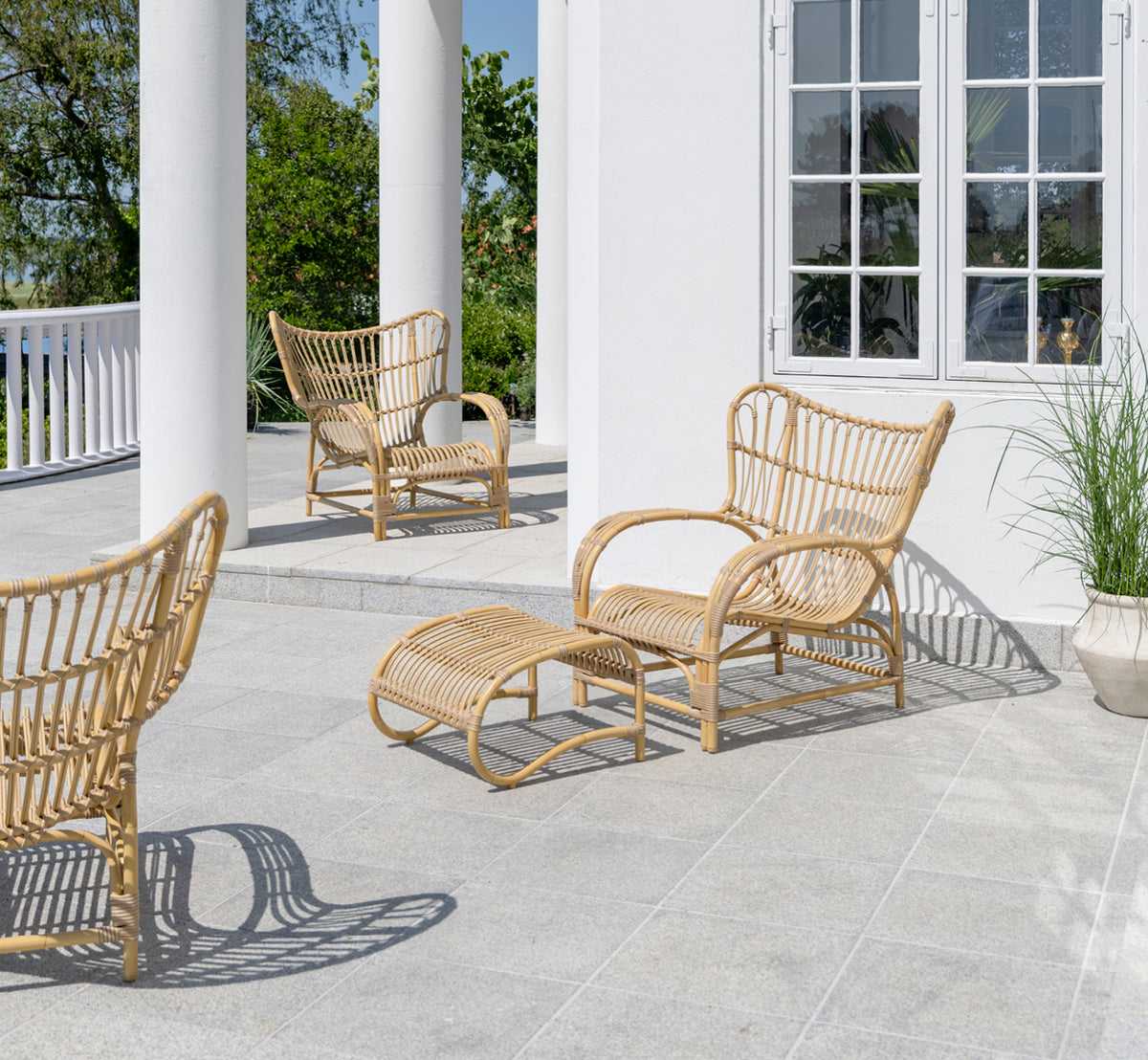 This is a lifestyle image of Teddy Exterior Footstool in natural aluminium artfibre. Paired with the matching lounge chair on a sunny paved terrace.