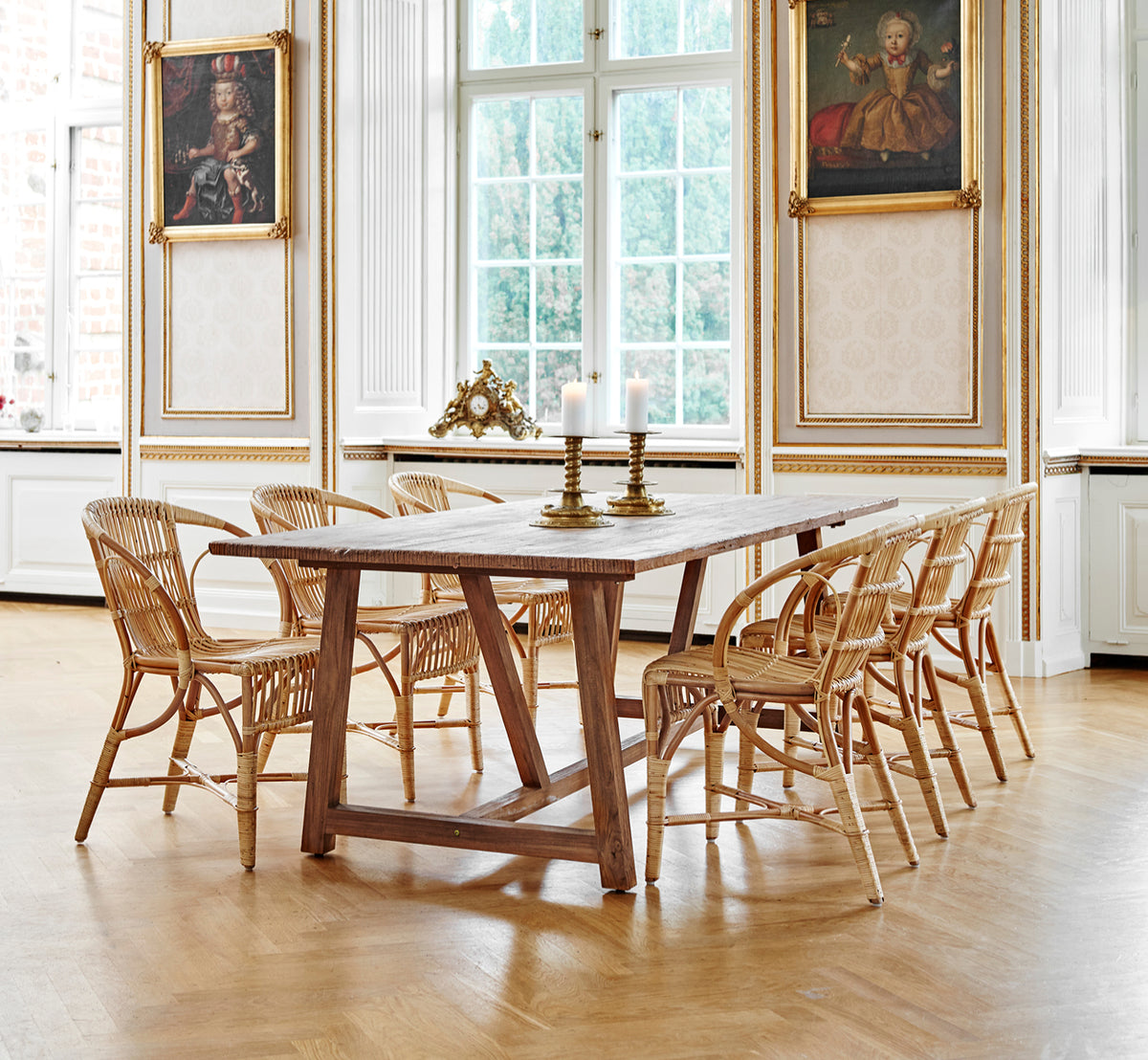 This is a lifestyle image of Robert Dining Chair in polished antique rattan. Placed beside a tall terracotta urn on a herringbone parquet floor.