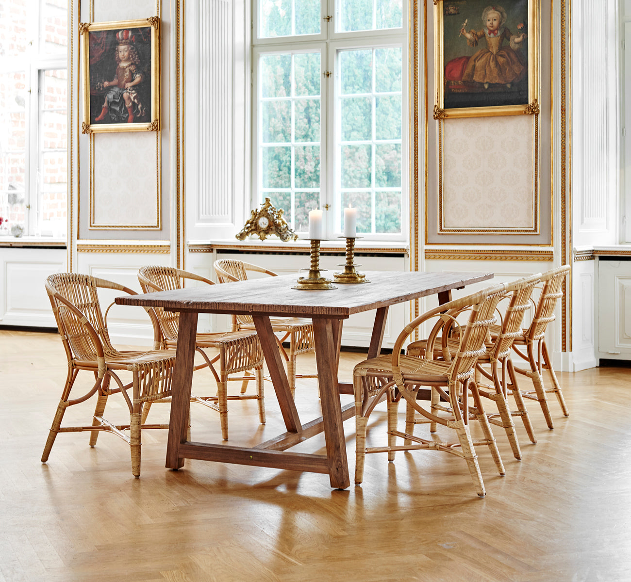 This is a lifestyle image of Robert Dining Chair in polished antique rattan. Placed beside a tall terracotta urn on a herringbone parquet floor.