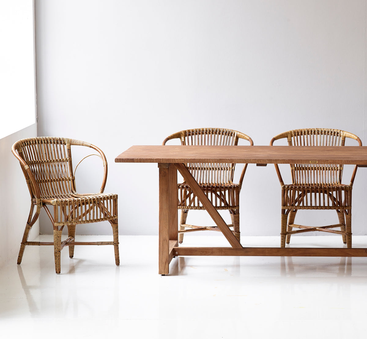 This is a lifestyle image of Robert Dining Chair in polished antique rattan. Placed beside a tall terracotta urn on a herringbone parquet floor.