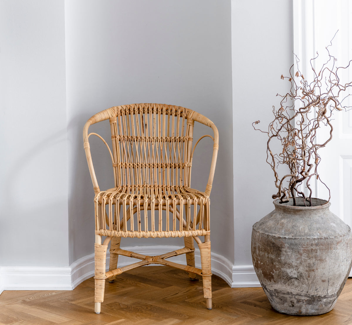 This is a lifestyle image of Robert Dining Chair in polished natural rattan. Placed beside a pedestal table with tulips on a jute rug.