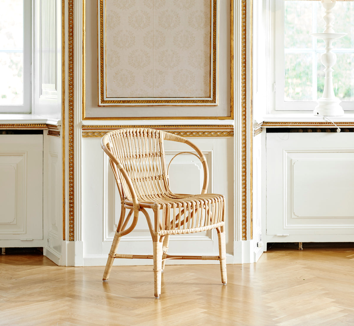 This is a lifestyle image of Robert Dining Chair in polished natural rattan. Placed beside a pedestal table with tulips on a jute rug.