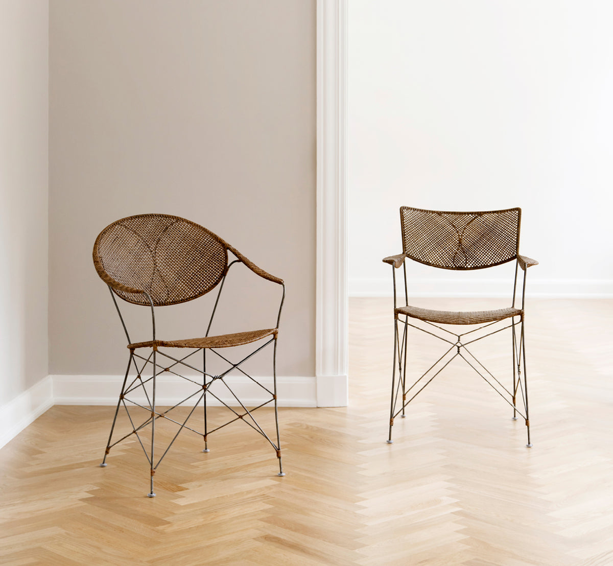 This is a lifestyle image of Rap Dining Chair in hazelnut rattan iron frame, in a bright interior with white panelled walls and herringbone parquet.