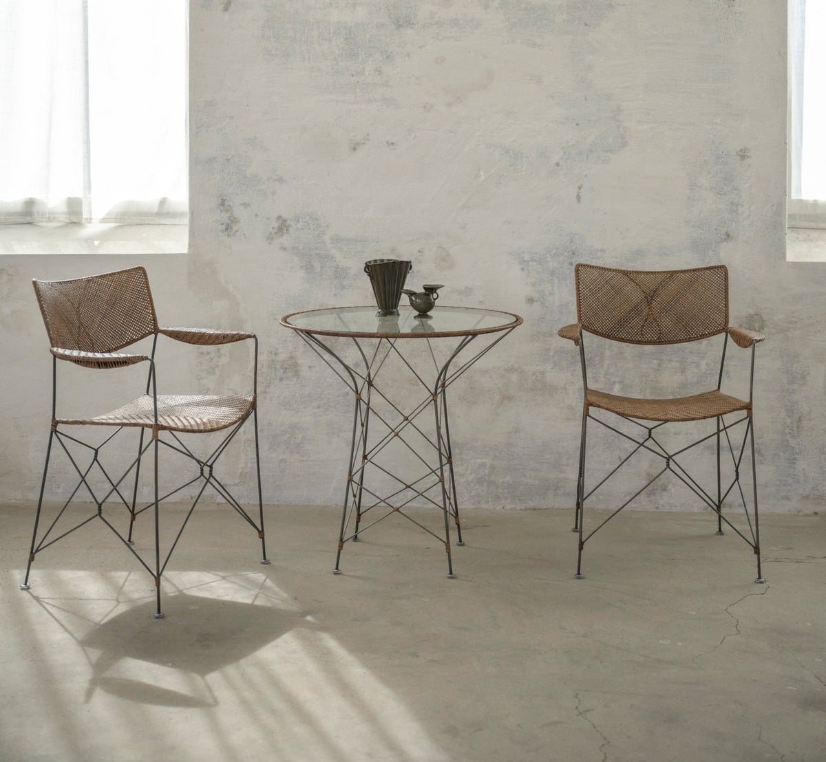 This is a lifestyle image of Funky Café Table in hazelnut rattan iron frame. With chairs in a pale, sunlit room.